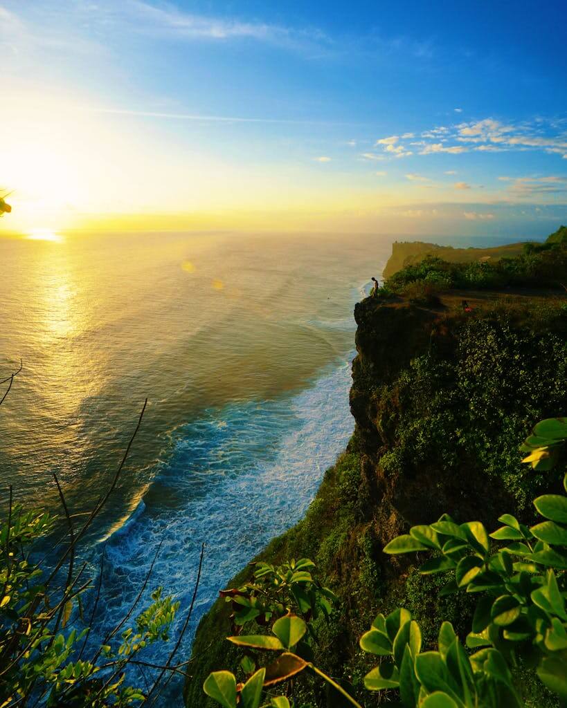 Breathtaking sunset view of the Bali coastline with lush green cliffs and ocean waves.