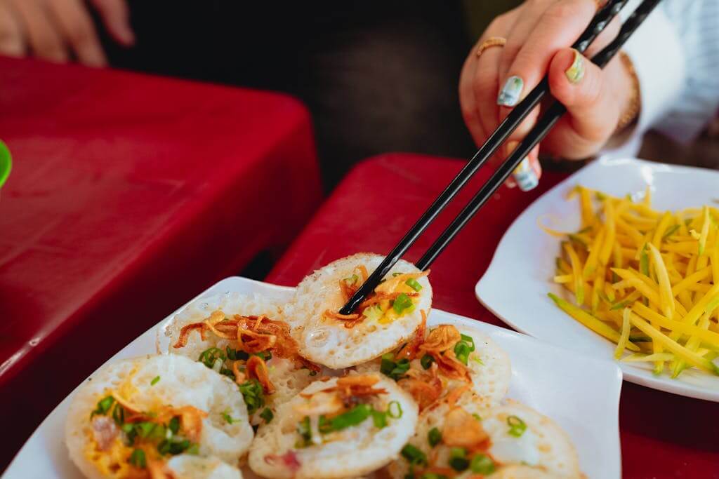 Close-up of Vietnamese street food, Bánh Khọt, with chopsticks on a red table.